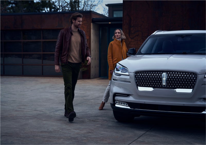 A man and a woman approaching a 2023 Lincoln Aviator® SUV, which illuminates certain lights when they are close | Mathews Lincoln in Marion OH