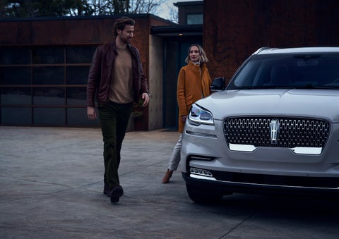 A man and a woman approaching a 2024 Lincoln Aviator® SUV, which illuminates certain lights when they are close | Mathews Lincoln in Marion OH