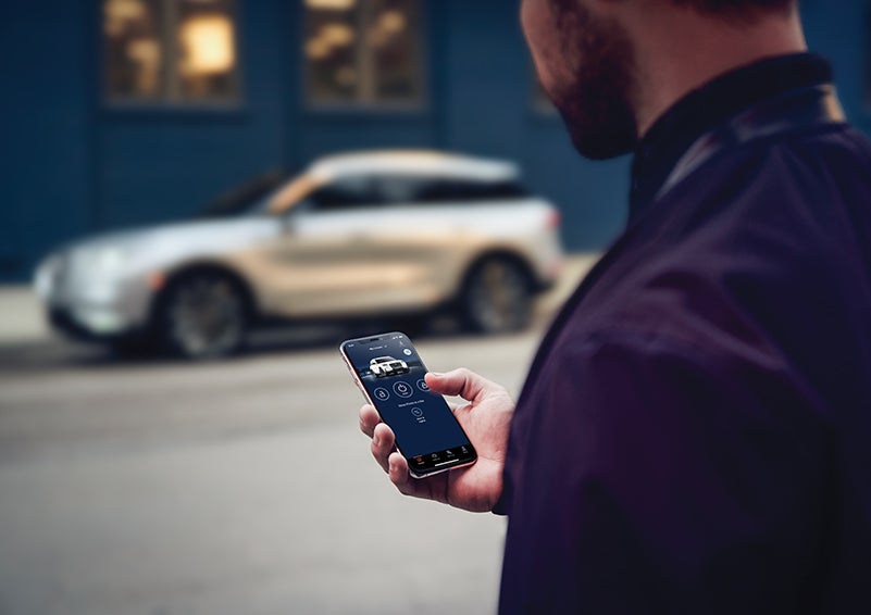 A person is shown interacting with a smartphone to connect to a Lincoln vehicle across the street. | Mathews Lincoln in Marion OH