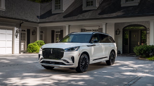 A white 2026 Lincoln Aviator® SUV is parked in the driveway of a luxury home. | Mathews Lincoln in Marion OH